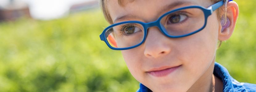 Close up of young caucasian boy with blue glasses and hearing aid